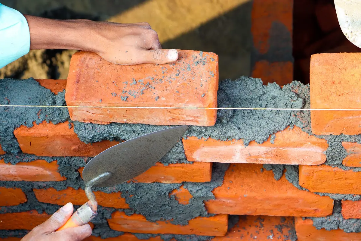 Maçon posant une brique à la truelle sur un chantier