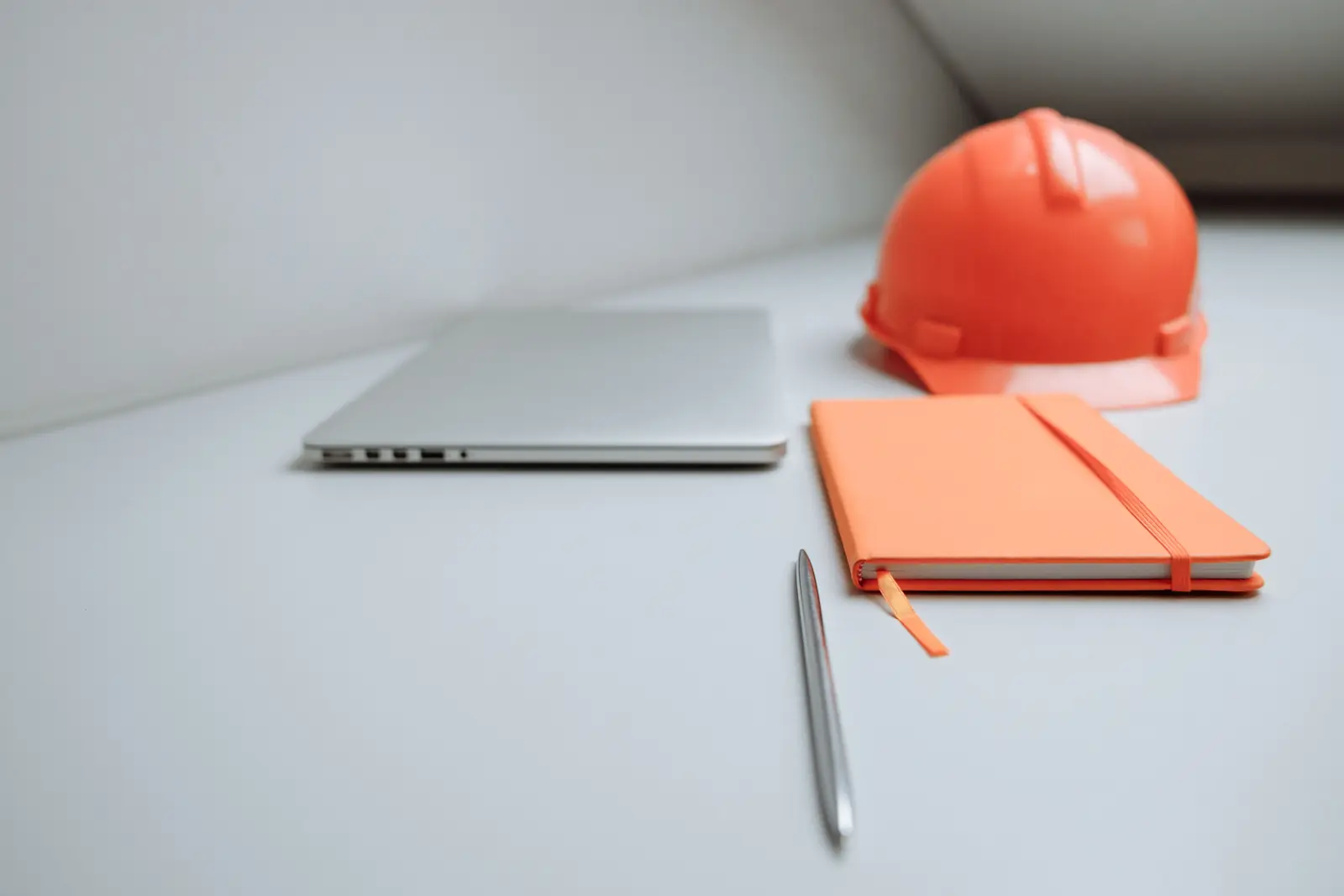 Ordinateur portable fermé et carnet de notes sur un bureau clair, casque de chantier orange en arrière-plan